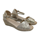 Sandalias de cuña Ramoncinas en piel metalizada dorada y suela de cáñamo sobre fondo blanco.