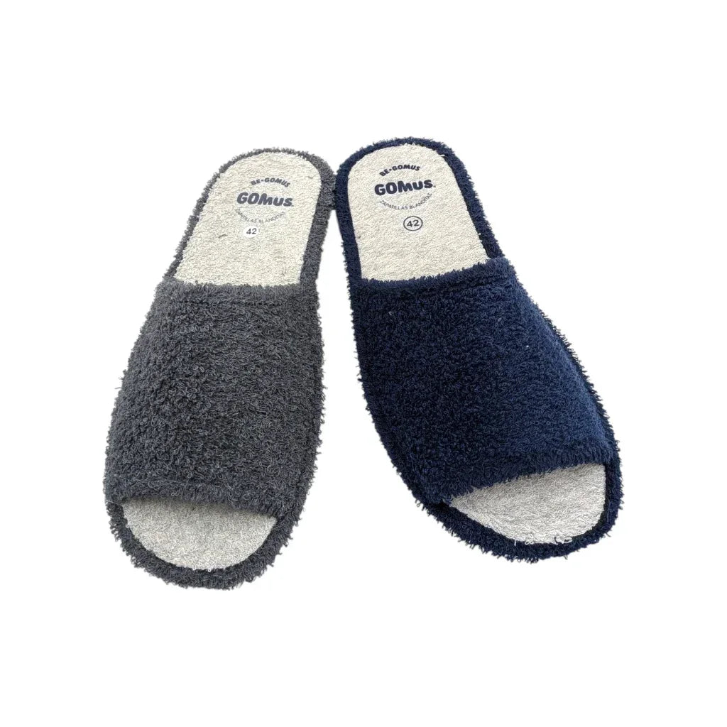 Primer plano de las zapatillas GOMUS abiertas para casa, disponibles en azul marino y gris antracita. Muestra la plantilla de rizo gris con logo y la textura esponjosa de toalla del empeine.
